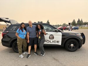 Three people pose in front of a Calgary Police car.